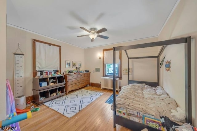 bedroom featuring radiator heating unit, wood finished floors, crown molding, and baseboards