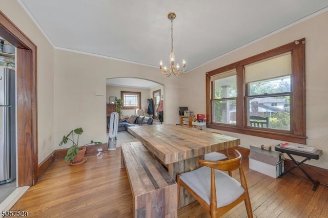 dining area featuring light wood-style floors, arched walkways, crown molding, a chandelier, and baseboards