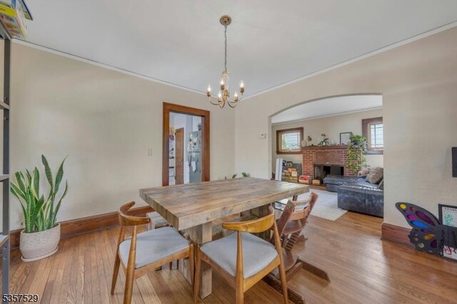 dining room featuring a chandelier, a fireplace, wood finished floors, ornamental molding, and baseboards