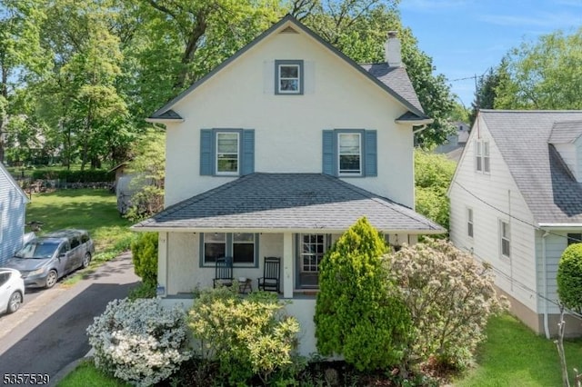 view of front of house with a chimney, roof with shingles, stucco siding, and covered porch