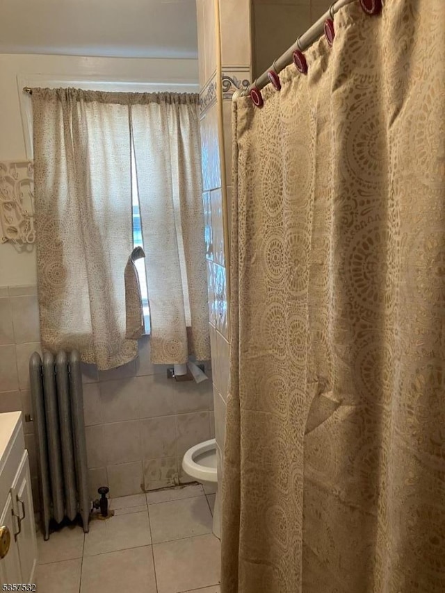 full bath with radiator heating unit, tile walls, tile patterned floors, toilet, and vanity