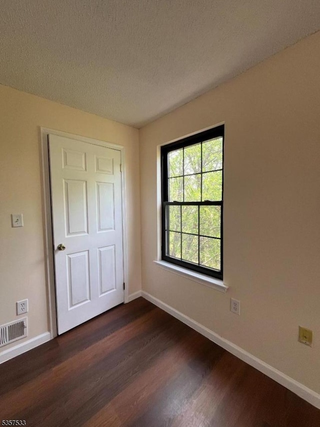 unfurnished bedroom with dark wood finished floors, baseboards, and a textured ceiling