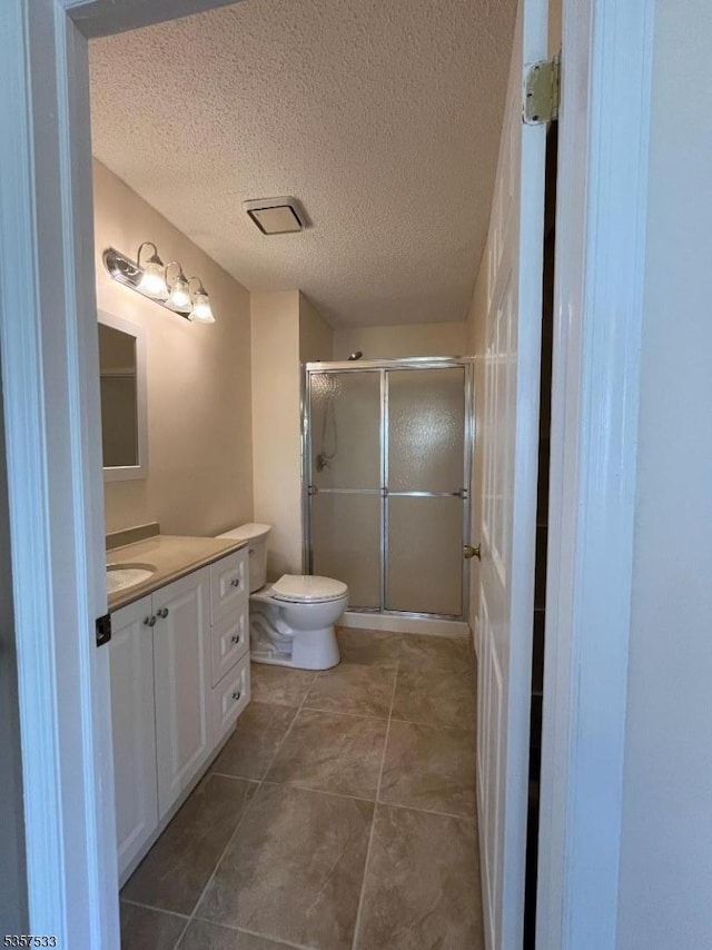 full bathroom featuring a stall shower, vanity, toilet, a textured ceiling, and tile patterned floors