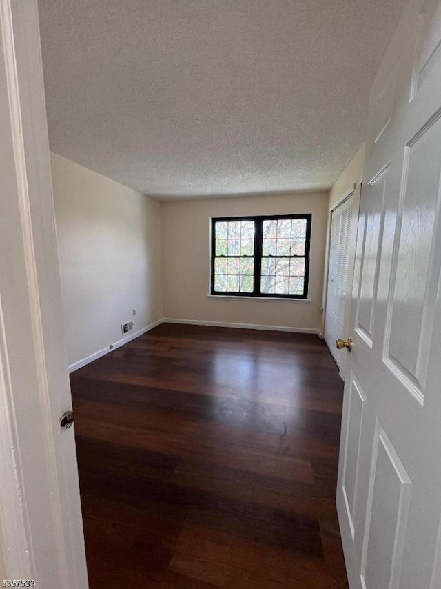 empty room with dark wood-style flooring, a textured ceiling, and baseboards
