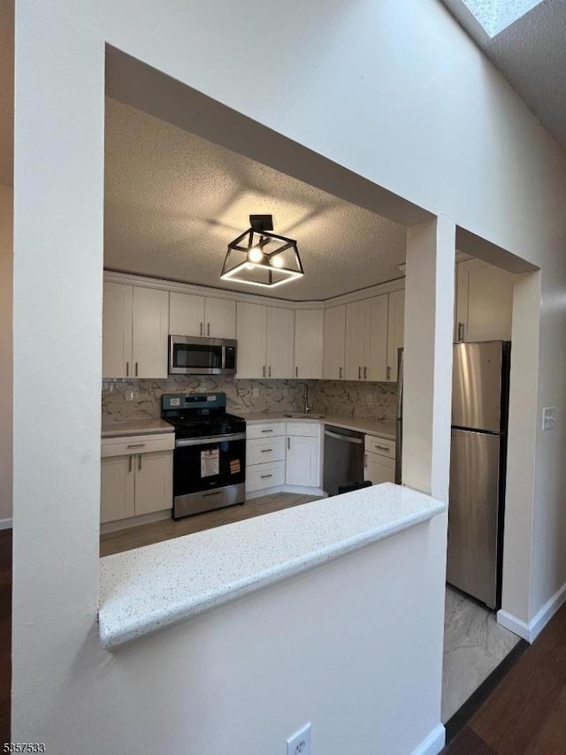 kitchen featuring stainless steel appliances, a textured ceiling, a sink, white cabinetry, and backsplash
