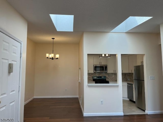 kitchen featuring a skylight, appliances with stainless steel finishes, backsplash, and wood finished floors