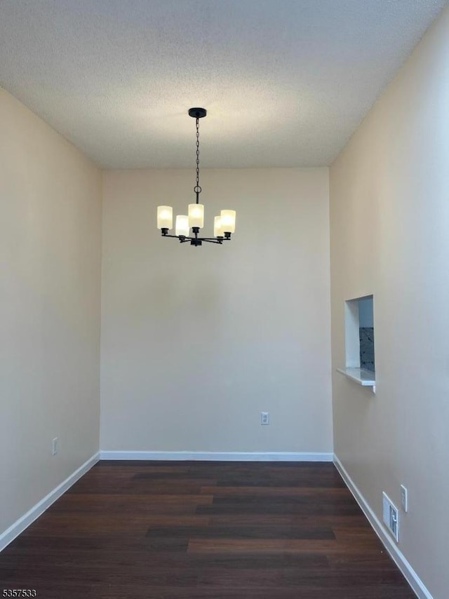 empty room featuring a chandelier, dark wood-style floors, and baseboards