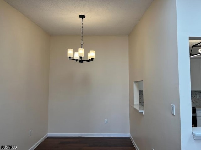 unfurnished room featuring a chandelier, dark wood-type flooring, and baseboards