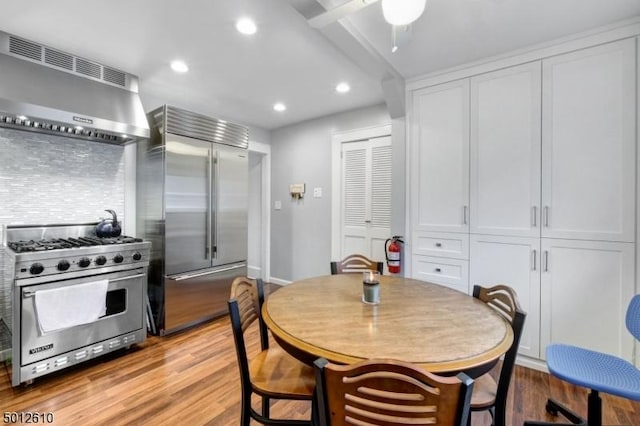 kitchen featuring high end appliances, exhaust hood, backsplash, white cabinets, and recessed lighting