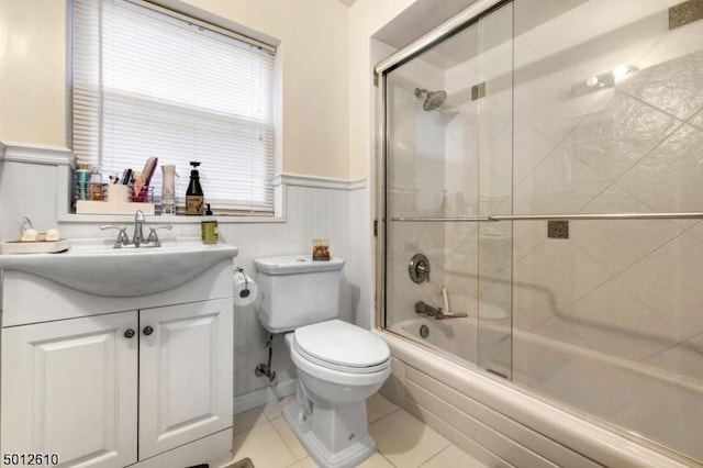 bathroom featuring toilet, wainscoting, vanity, bath / shower combo with glass door, and tile patterned flooring