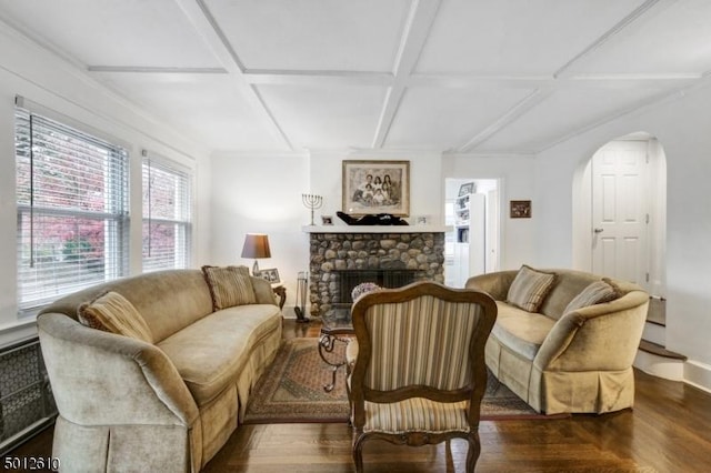 living room with coffered ceiling, a stone fireplace, arched walkways, baseboards, and wood finished floors