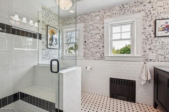 full bath featuring radiator, tile walls, a stall shower, vanity, and wainscoting