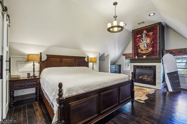 bedroom featuring vaulted ceiling, dark wood-style flooring, a stone fireplace, a chandelier, and recessed lighting