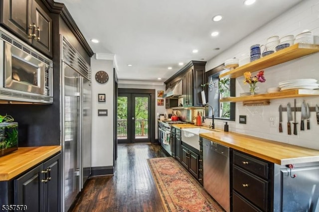 kitchen featuring wood counters, built in appliances, open shelves, dark wood finished floors, and extractor fan