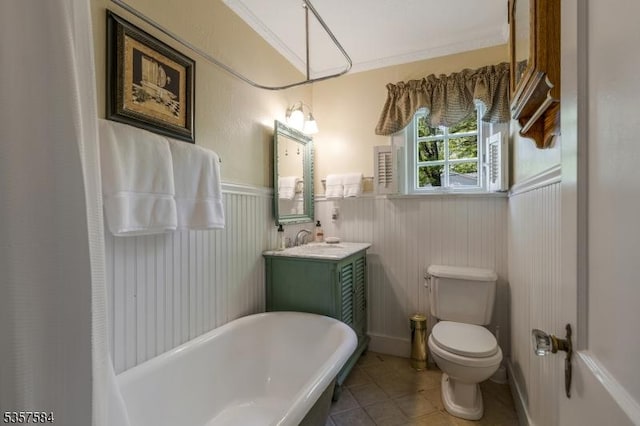 full bathroom featuring toilet, a freestanding tub, a wainscoted wall, tile patterned floors, and vanity