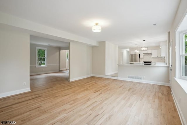 unfurnished living room featuring light wood-style floors, plenty of natural light, a chandelier, and baseboards