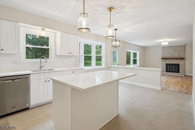 kitchen with dishwasher, a sink, a kitchen island, a brick fireplace, and white cabinets