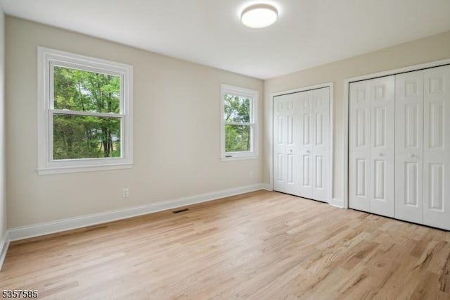 unfurnished bedroom featuring multiple closets, light wood-style flooring, and baseboards