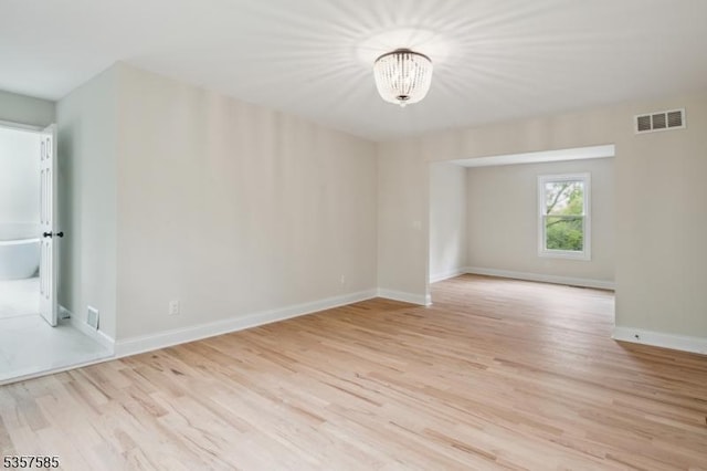 empty room with a chandelier, light wood-style flooring, and baseboards