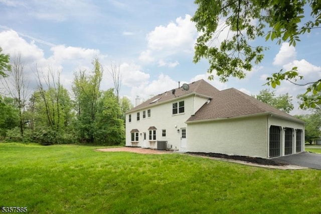 rear view of house featuring stucco siding, a yard, an attached garage, central AC, and asphalt driveway
