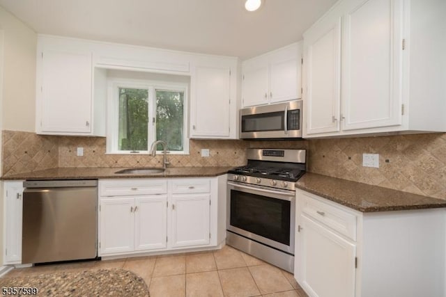 kitchen featuring appliances with stainless steel finishes, a sink, white cabinets, dark stone countertops, and light tile patterned floors