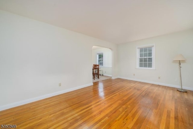 empty room featuring arched walkways, light wood-style flooring, and baseboards