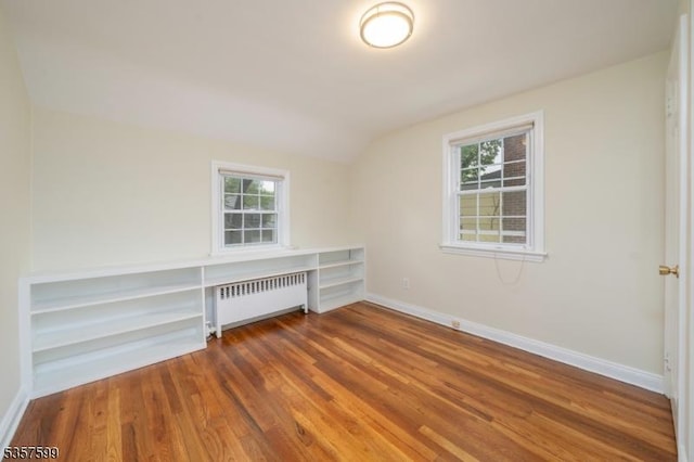 spare room featuring radiator heating unit, lofted ceiling, wood finished floors, and baseboards