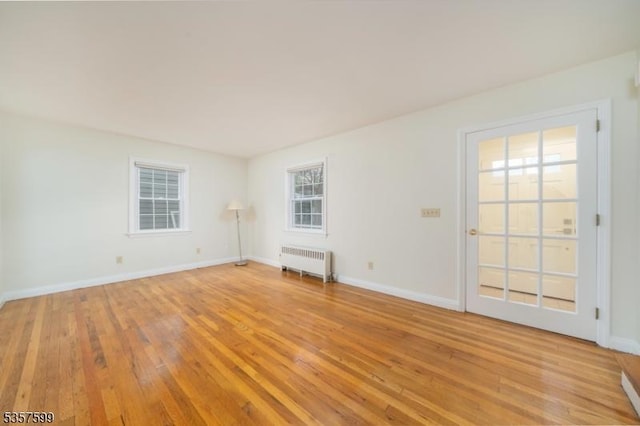 spare room with radiator heating unit, light wood finished floors, and baseboards