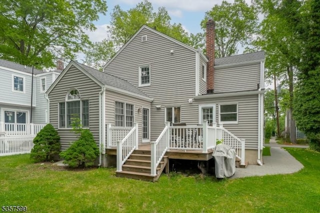 back of house featuring a chimney, a yard, a wooden deck, and roof with shingles