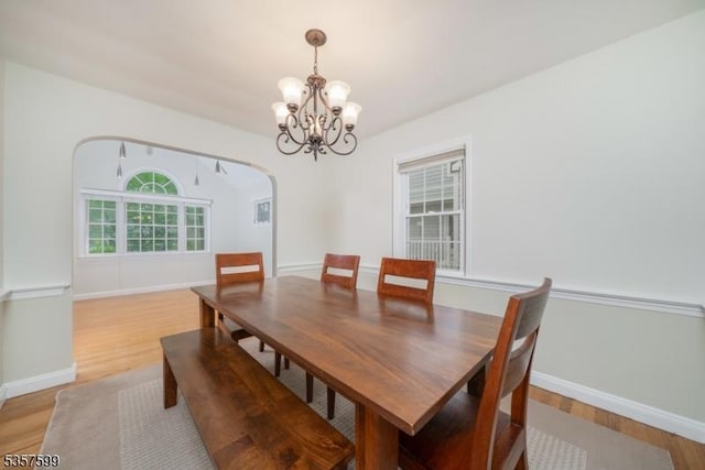 dining space with light wood-type flooring, a chandelier, arched walkways, and baseboards