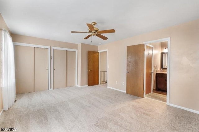 unfurnished bedroom featuring multiple closets, light colored carpet, ensuite bath, baseboards, and ceiling fan