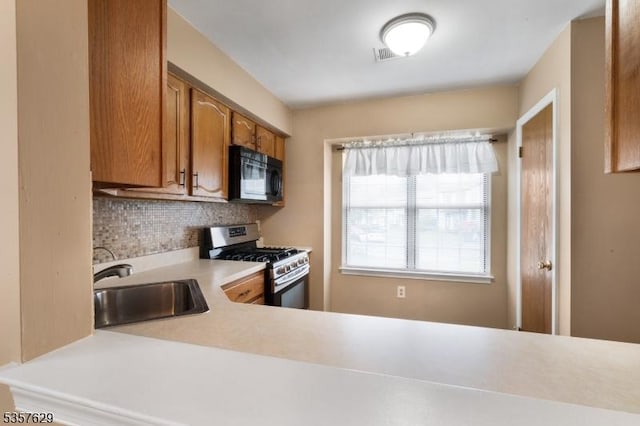 kitchen with black microwave, stainless steel gas stove, a sink, brown cabinets, and light countertops