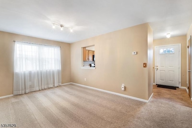 unfurnished room featuring light carpet, healthy amount of natural light, baseboards, and rail lighting