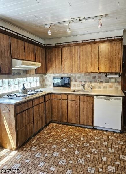 kitchen featuring white appliances, a sink, under cabinet range hood, and backsplash
