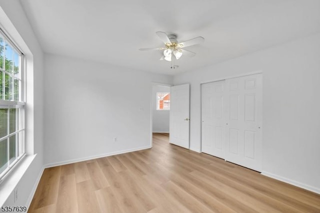 unfurnished bedroom featuring multiple windows, light wood-type flooring, and baseboards