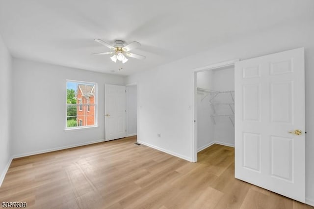 unfurnished bedroom featuring baseboards, light wood-type flooring, a walk in closet, a closet, and a ceiling fan