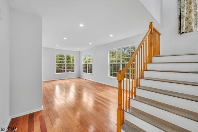 unfurnished living room with healthy amount of natural light, stairs, baseboards, light wood-style flooring, and recessed lighting