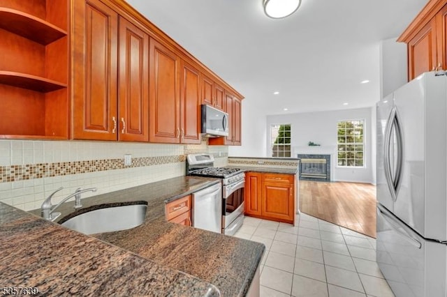 kitchen featuring stainless steel appliances, a sink, light tile patterned floors, decorative backsplash, and brown cabinetry