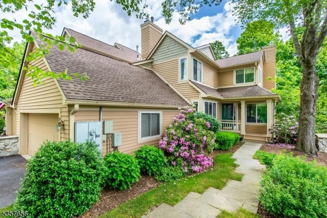 view of front of home featuring a chimney, a shingled roof, a garage, and covered porch