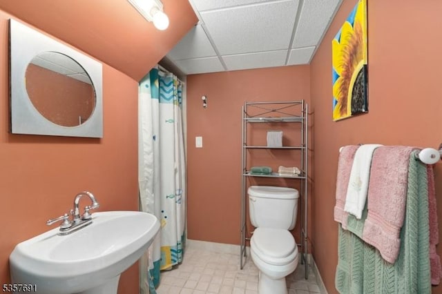 full bath featuring a sink, toilet, a paneled ceiling, a shower with shower curtain, and baseboards