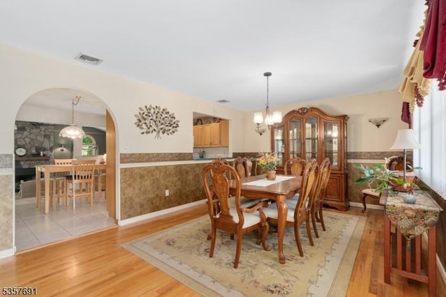 dining space with arched walkways, wainscoting, light wood finished floors, and a chandelier