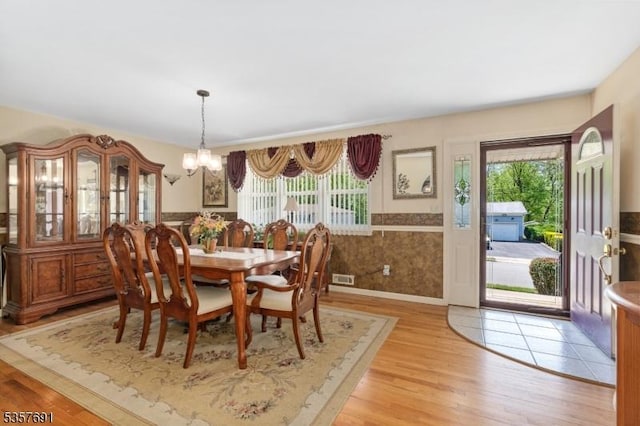 dining area with plenty of natural light, a chandelier, light wood-type flooring, and wainscoting