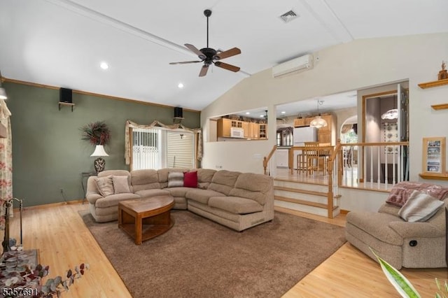 living area featuring a wall unit AC, lofted ceiling, wood finished floors, ceiling fan, and stairway