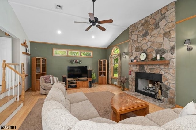 living area featuring wood finished floors, ceiling fan, vaulted ceiling, a fireplace, and stairs