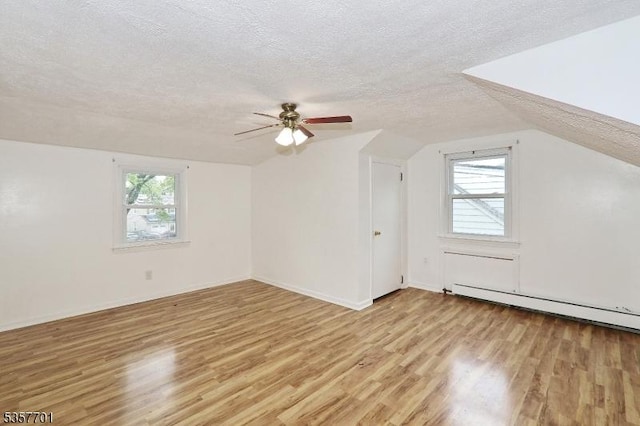 additional living space with a textured ceiling, light wood-style floors, plenty of natural light, vaulted ceiling, and a ceiling fan
