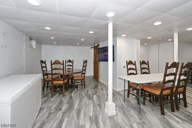 dining area with light wood-style flooring, recessed lighting, a barn door, baseboards, and a drop ceiling
