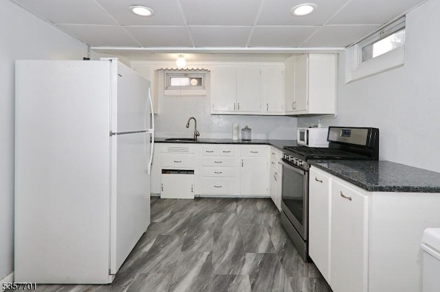 kitchen with white appliances, dark countertops, white cabinets, a drop ceiling, and a sink