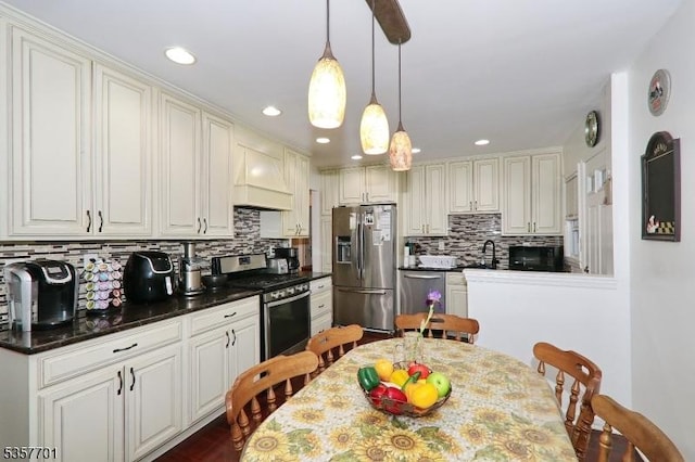 kitchen with appliances with stainless steel finishes, premium range hood, backsplash, decorative light fixtures, and dark countertops