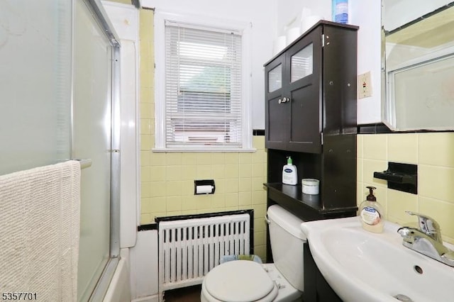 full bath with radiator heating unit, tile walls, a sink, a shower with door, and toilet