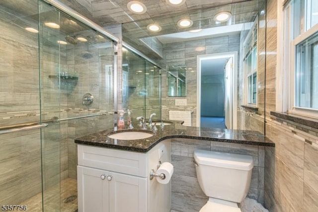 bathroom featuring tile walls, a shower stall, toilet, and vanity
